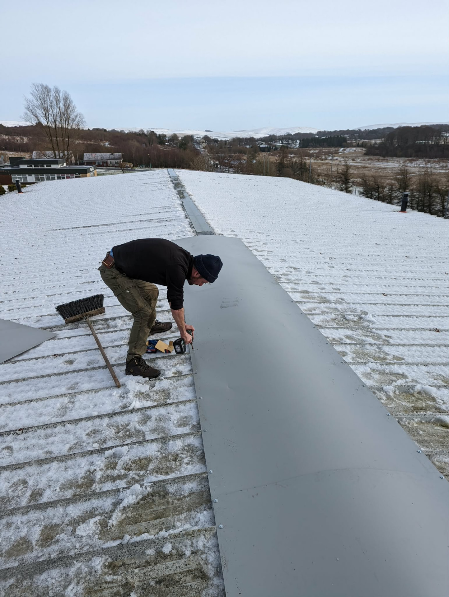 Roofer fitting a metal ridge cap on a sheet roof in winter